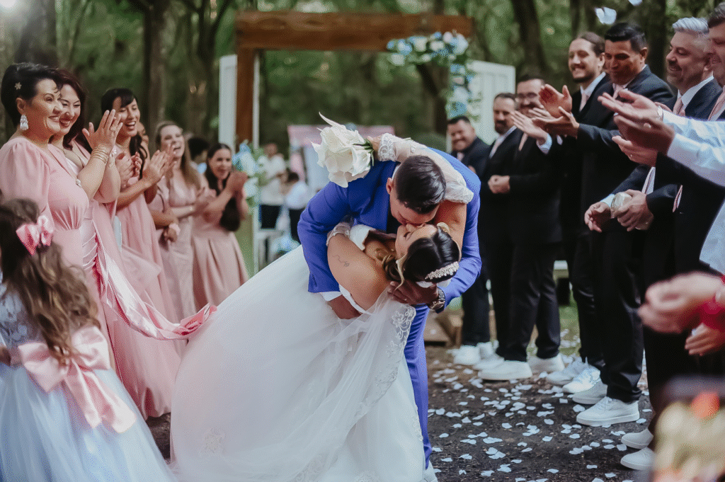 Imagem de um casal se beijando com os padrinhos ao lado sorindo e aplaudindo