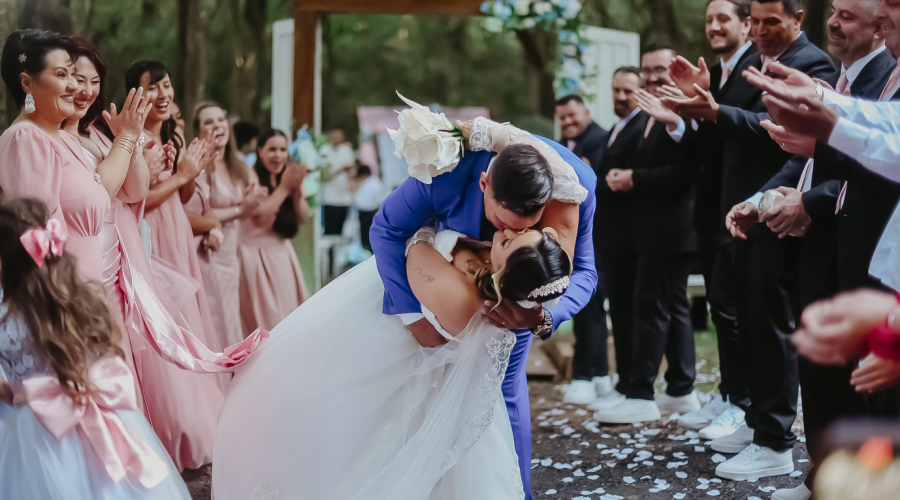 Imagem de um casal se beijando com os padrinhos ao lado sorindo e aplaudindo